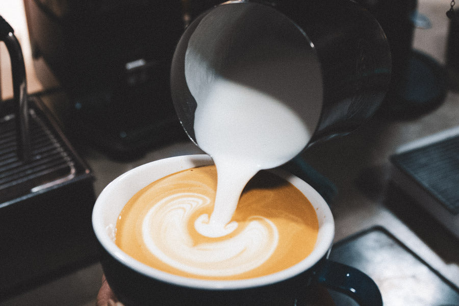 Pouring milk into a cup of coffee to create latte art.