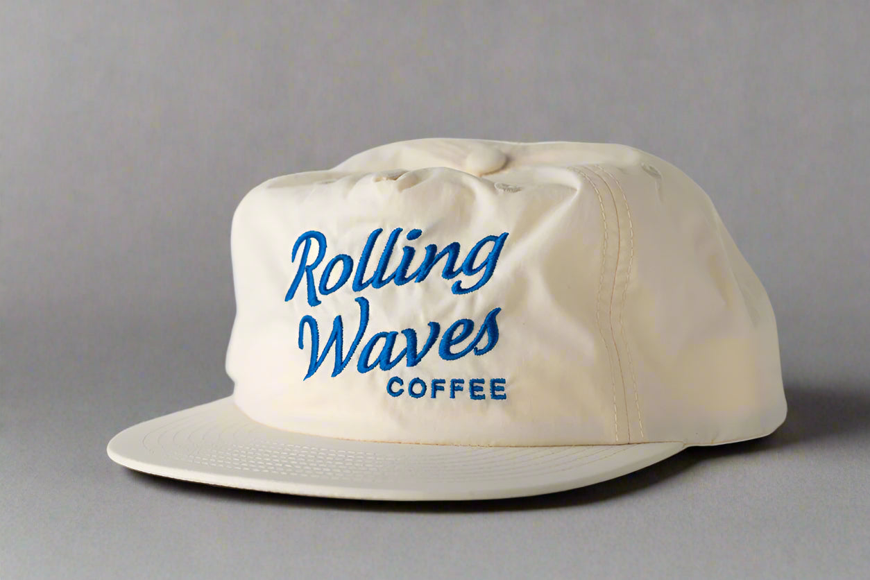 Beige cap with 'Rolling Waves Coffee' text on a light gray background